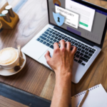 hand typing on a laptop, other holds a coffee, cyber security on the laptop screen